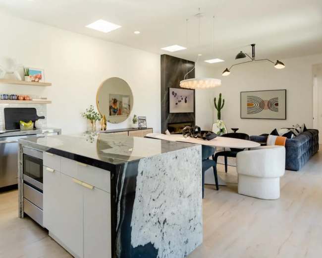 A modern kitchen features a large island with a marble countertop and sleek cabinetry, with an adjacent dining area furnished with contemporary seating and artwork.