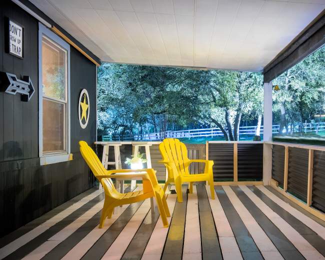 The image features a porch with two yellow chairs, a small table, and illuminated trees in the background.
