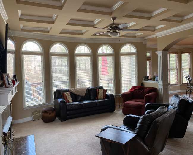 A spacious living room with a coffered ceiling, large arched windows, and a mix of black leather and red upholstered furniture.
