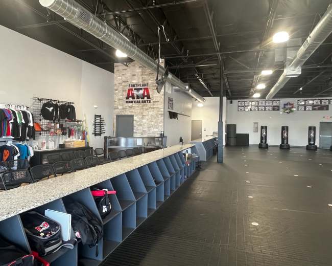 The image shows an interior view of a martial arts studio with a reception area, seating, and training mats.