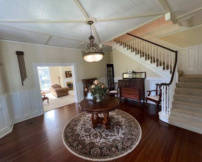 A spacious foyer with a round table and a floral arrangement, featuring a staircase that leads to an upper level.