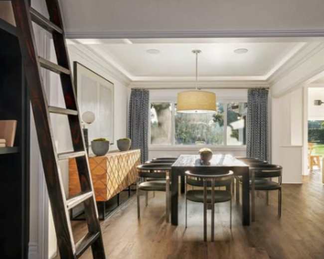 A dining room features a wooden table surrounded by chairs, a pendant light, and large windows with outdoor views.
