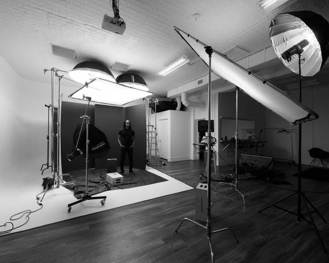 A photography studio is set up with various lighting equipment and a model positioned in the center.
