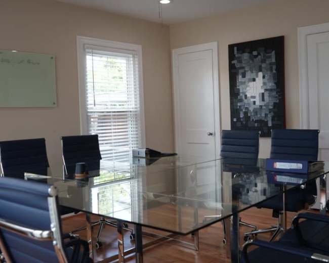 A modern conference room features a glass table surrounded by blue chairs and a whiteboard on the wall.
