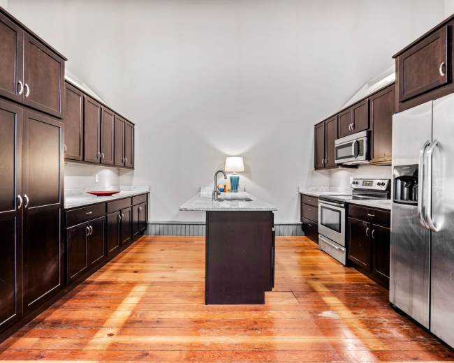 A modern kitchen features dark wooden cabinetry, stainless steel appliances, and a central island with a light-colored countertop, set against a hardwood floor.