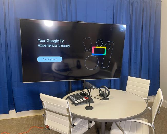 A television screen displays a message indicating that the Google TV experience is ready, set in a room with a round table and chairs.