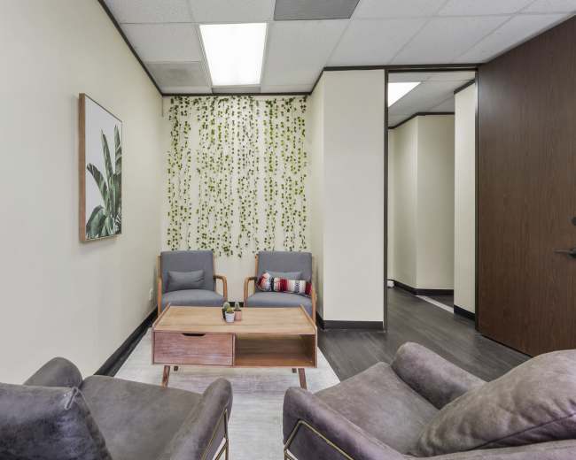 The image shows a small waiting area with two armchairs, a coffee table, and a plant-themed backdrop on the wall.
