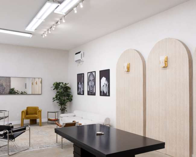 The image shows a minimalist interior space featuring a large black table, framed artwork on the walls, and a decorative arch structure.