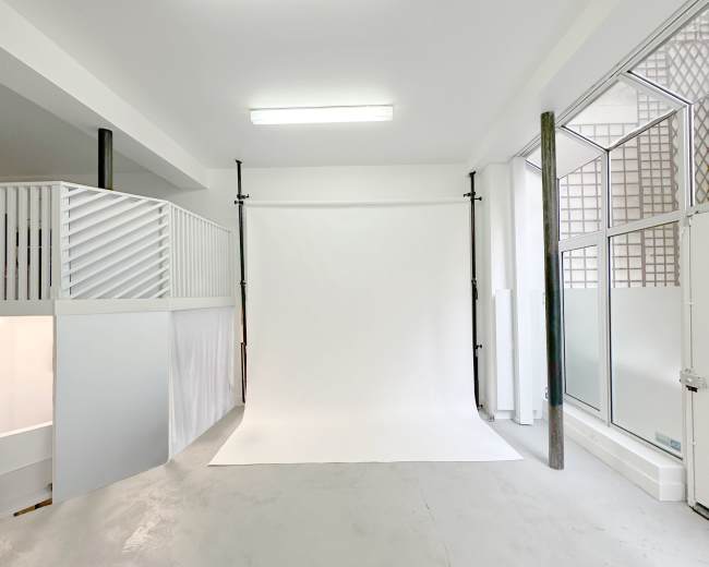 The image shows a well-lit photography studio with a white backdrop and plain gray flooring.