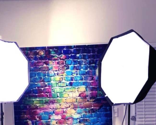 The image shows two large softbox lights positioned in front of a colorful brick wall.