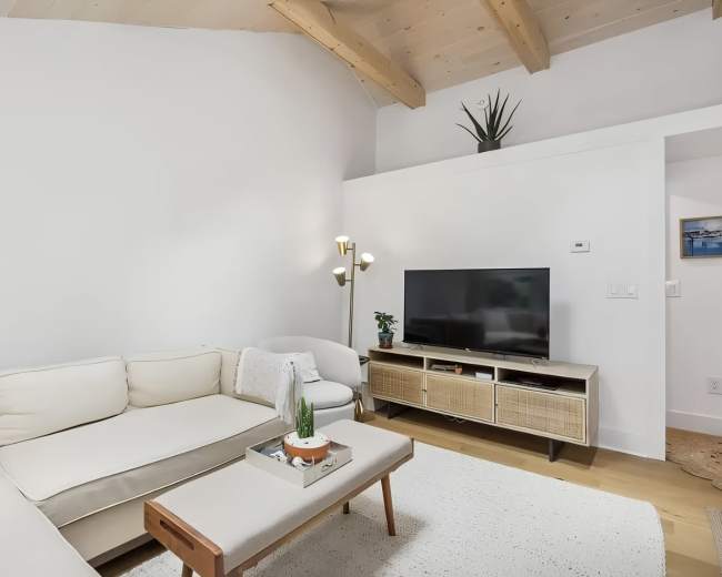 The living room features a sectional sofa, a television on a stand, and a light-colored rug under a vaulted ceiling.