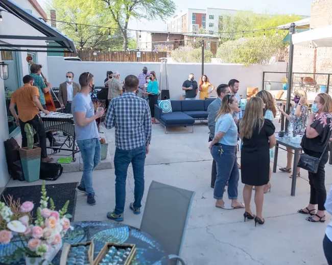 A group of people socialize in an outdoor patio area, some wearing masks, while a small band performs in the background.