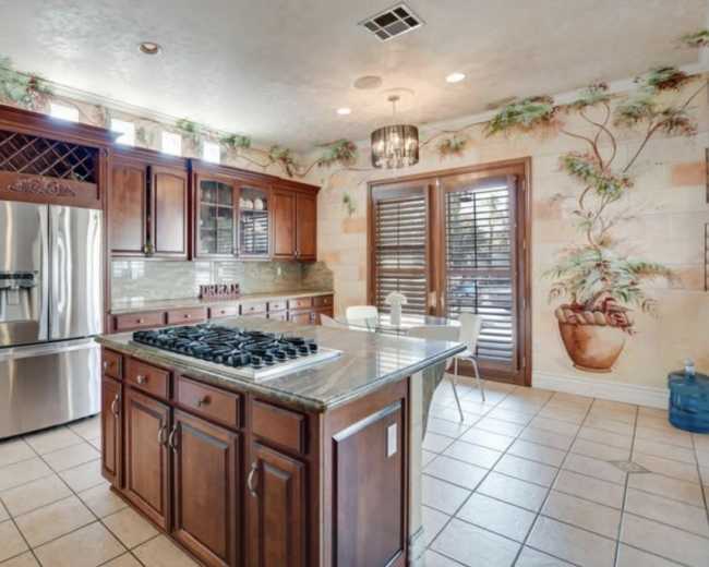 The living room features a patterned sofa, two upholstered chairs, a coffee table, and decorative elements against a backdrop of warm-painted walls and plantation shutters.