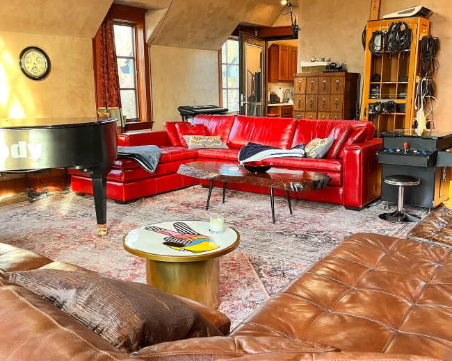 A cozy living room with red leather sofas, a grand piano, and various musical equipment.