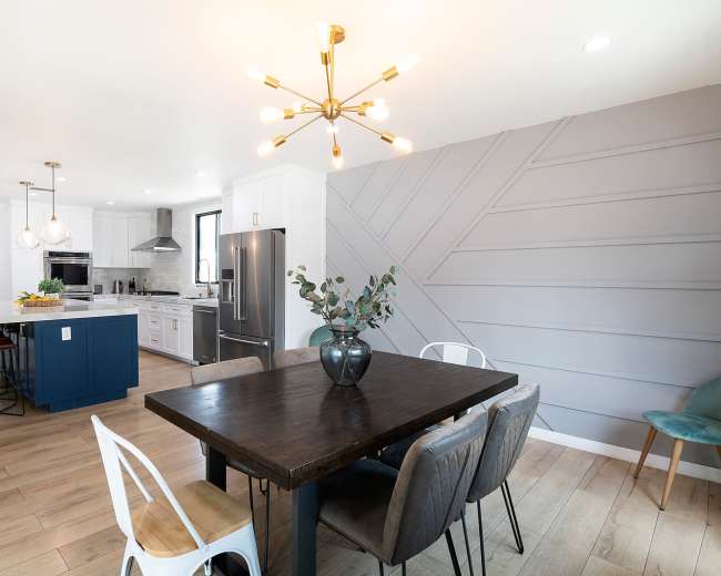 A contemporary kitchen features a large dining table, modern lighting fixtures, and a mix of cabinetry and appliances.