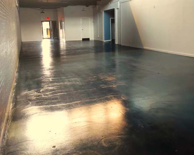The image shows a long, empty hallway with polished floors and natural light streaming in from windows at the far end.