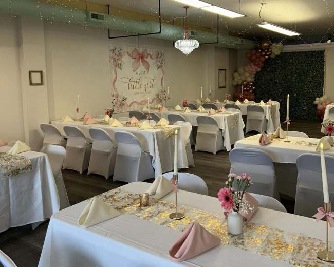 The image shows a decorated event space with neatly arranged tables, each set with white tablecloths and pink napkins, and adorned with candles, flowers, and a backdrop featuring a "Cattle Girl" theme.