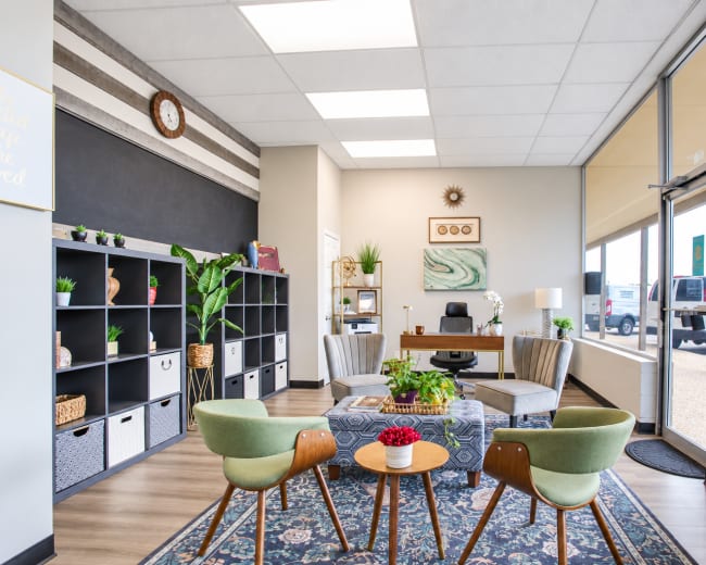 The image shows a modern office reception area featuring a seating arrangement with green chairs and a decorative table, along with shelves and a desk.