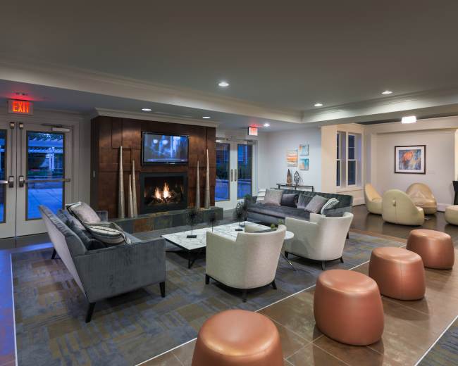 The image shows a modern lounge area featuring comfortable seating, a fireplace, and a bar in the background.