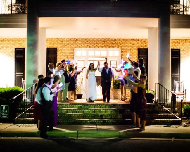 A bride and groom exit a building as guests hold colorful sparklers in celebration.