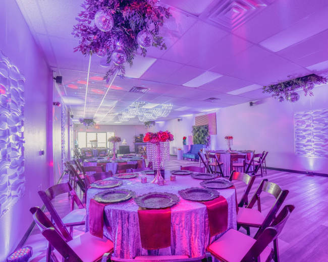 A brightly lit event space features round tables set with colorful tableware and floral arrangements under decorative lighting.