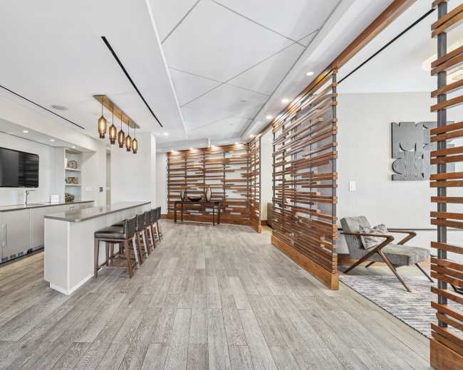 The image shows a modern interior space featuring a kitchen island with barstools, a living area with a chair, and decorative wooden dividers separating different sections.