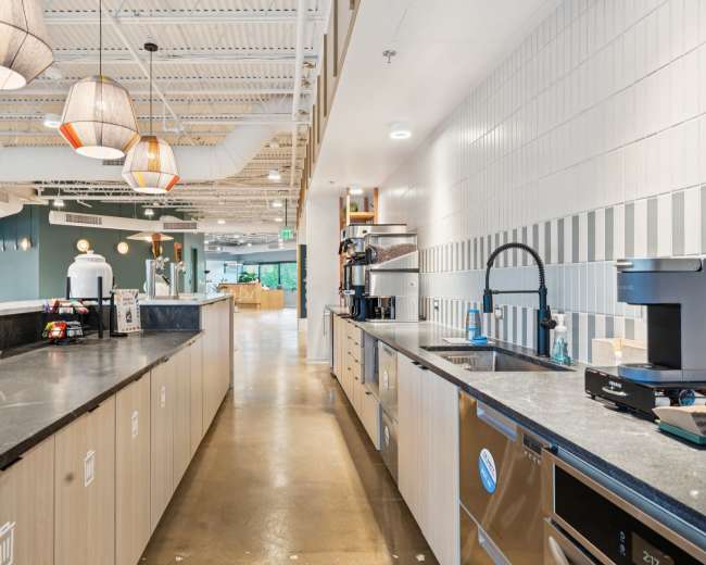 The image shows a modern kitchen space with a long counter, coffee machines, and pendant lights hanging from the ceiling.
