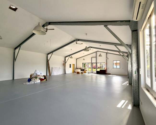 The image shows a spacious, empty room with high ceilings, large windows, and a smooth, gray floor.