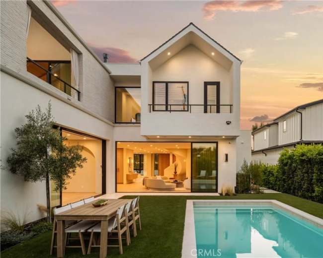 The image shows a modern two-story house with large glass doors opening to a backyard featuring a swimming pool and a dining area.