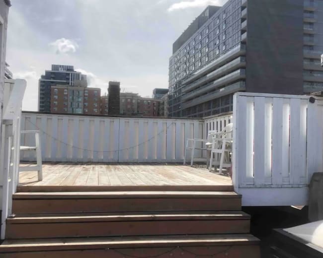 A rooftop deck with wooden steps leading up to it, surrounded by modern apartment buildings in the background.