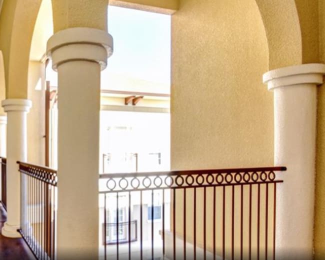 The image shows a corridor with archways, white columns, and a decorative black bench along one side.