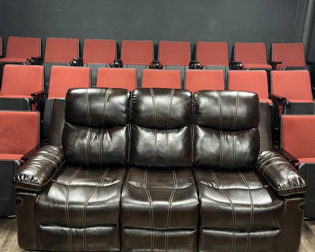 A brown leather couch with three seats is positioned in front of a row of red theater-style seats in a screening room.