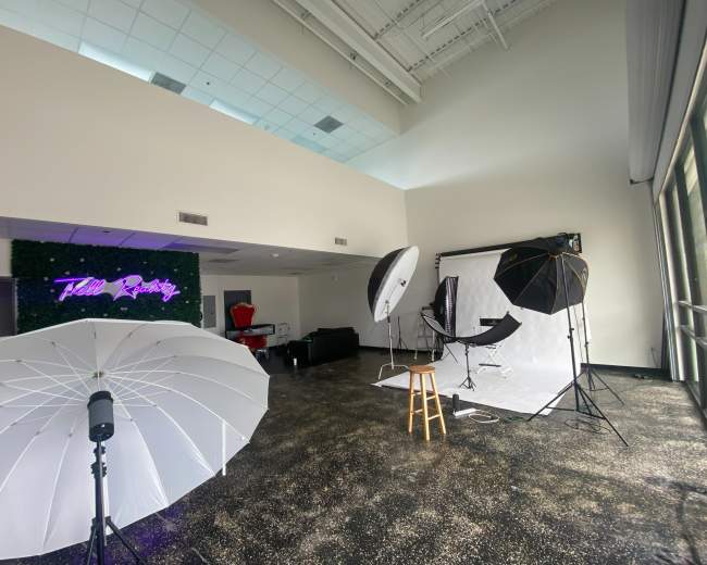 A photography studio setup with lighting equipment and a backdrop, featuring a neon sign that reads "Hello Reality."