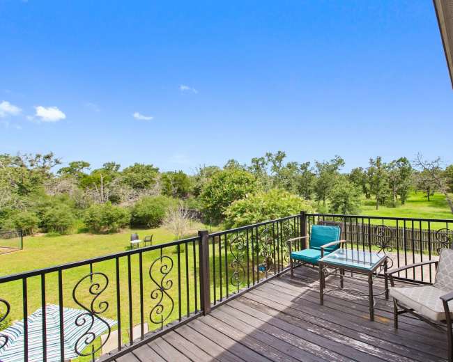 A spacious outdoor balcony with two chairs and a table, overlooking a green landscape with trees.