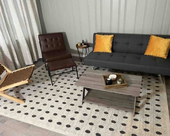 A modern living room setup with a gray sofa, a brown chair, a round side table, and a patterned area rug.