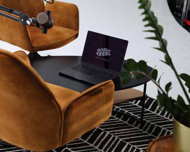 A workspace is set up with two brown armchairs, a laptop on a table, and a plant nearby, all arranged on a patterned rug.