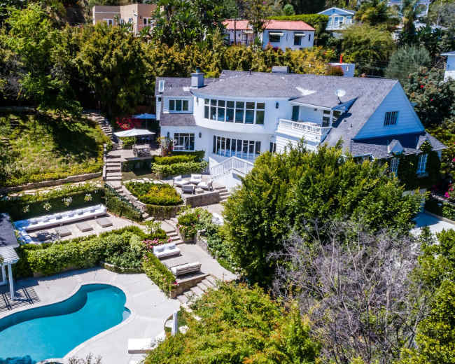 The image shows a spacious house with a swimming pool surrounded by landscaped greenery and outdoor seating areas.