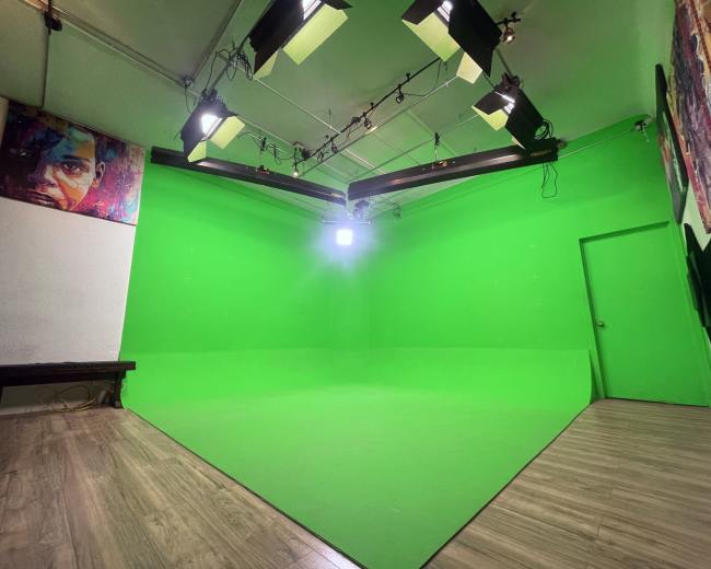 The image shows a green screen studio with bright lights and a wooden floor.