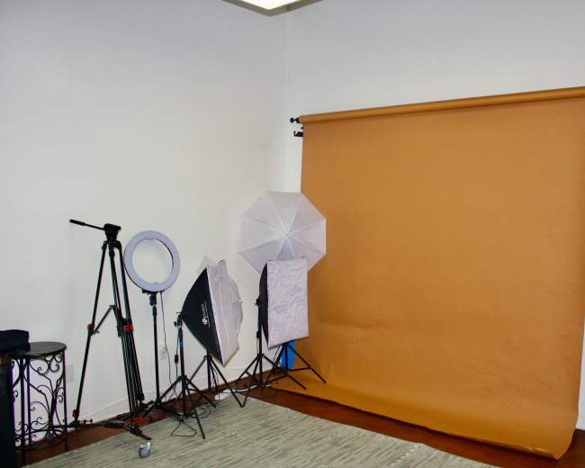 The image shows a photography studio setup with a brown backdrop and various lighting equipment, including umbrellas and a ring light.
