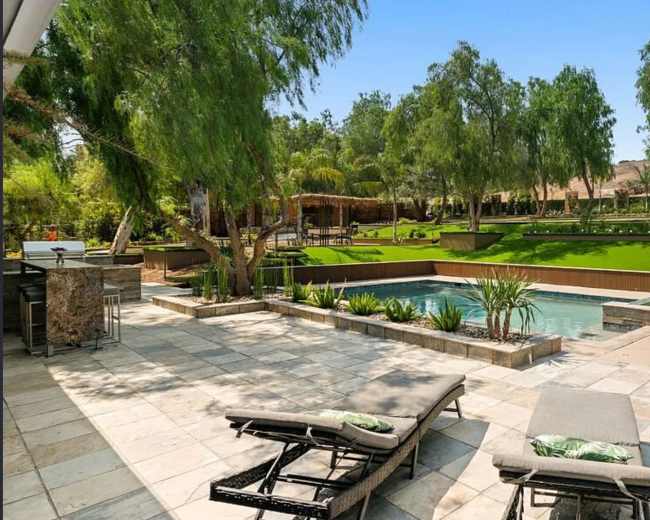 The image shows a modern backyard with a swimming pool, lounging chairs, and landscaped greenery.