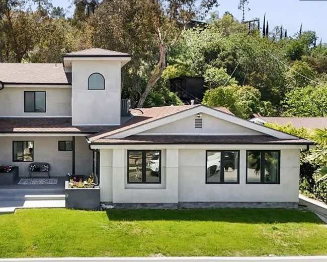 The image shows a modern two-story house with a landscaped front yard and a balcony on the upper level.