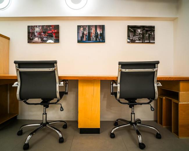 The image shows two black office chairs facing a wooden desk with three framed photographs hanging on the wall above.
