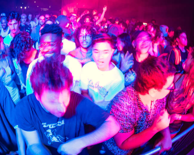 A crowd of people enjoys a lively music performance under colorful stage lighting.