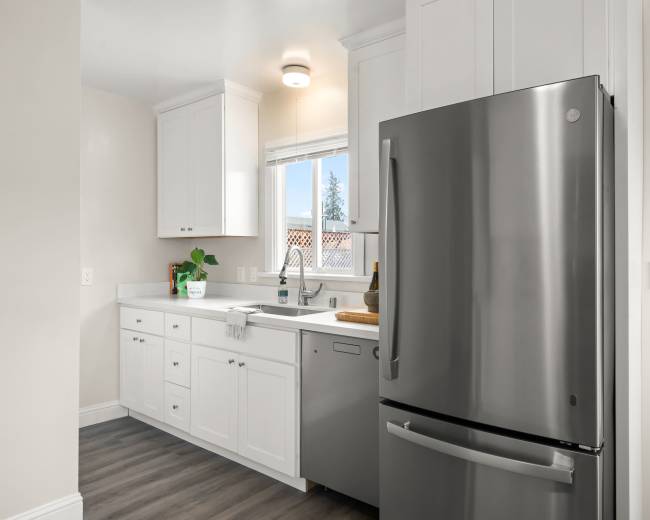 A modern kitchen with white cabinets, a stainless steel refrigerator, and a window above the sink.