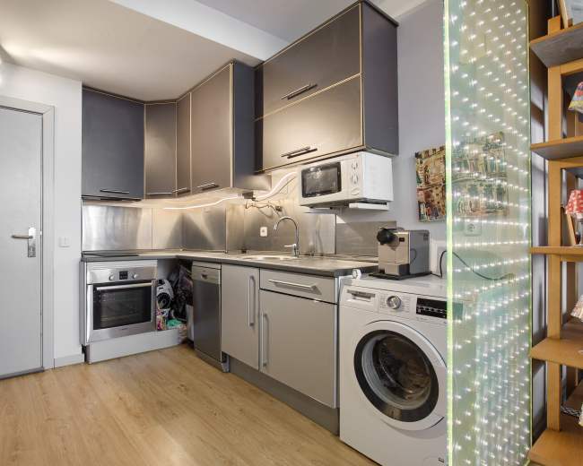 A compact kitchen featuring modern appliances, including a refrigerator, oven, microwave, and washing machine, with a lighted decorative panel on the right.