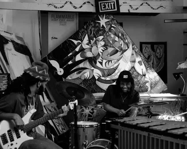 A band performs in an art studio surrounded by large, colorful paintings.