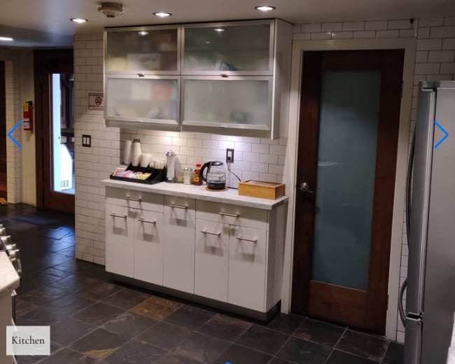 A modern kitchen with white cabinets, a countertop, and a door leading to another room.