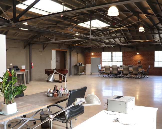 A spacious industrial-style office with high ceilings, a conference area, and various workstations.