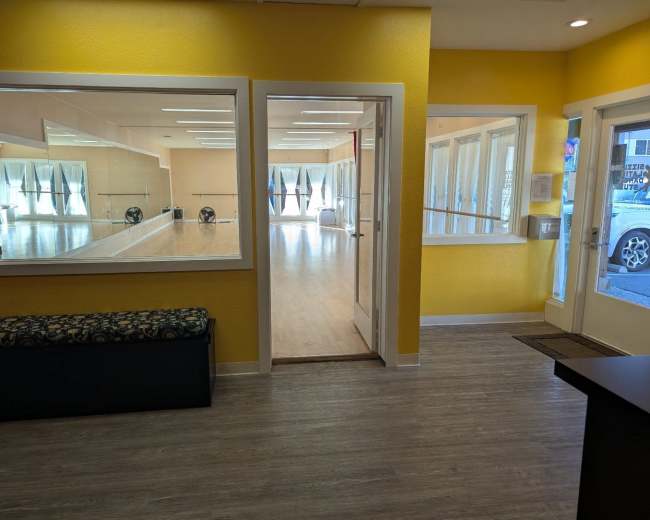 The image shows a brightly lit entryway with yellow walls leading into a mirrored dance studio.