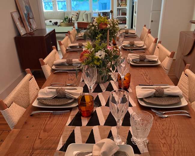 A long wooden dining table is set with elegant tableware, including glassware and decorative centerpieces, ready for a meal.